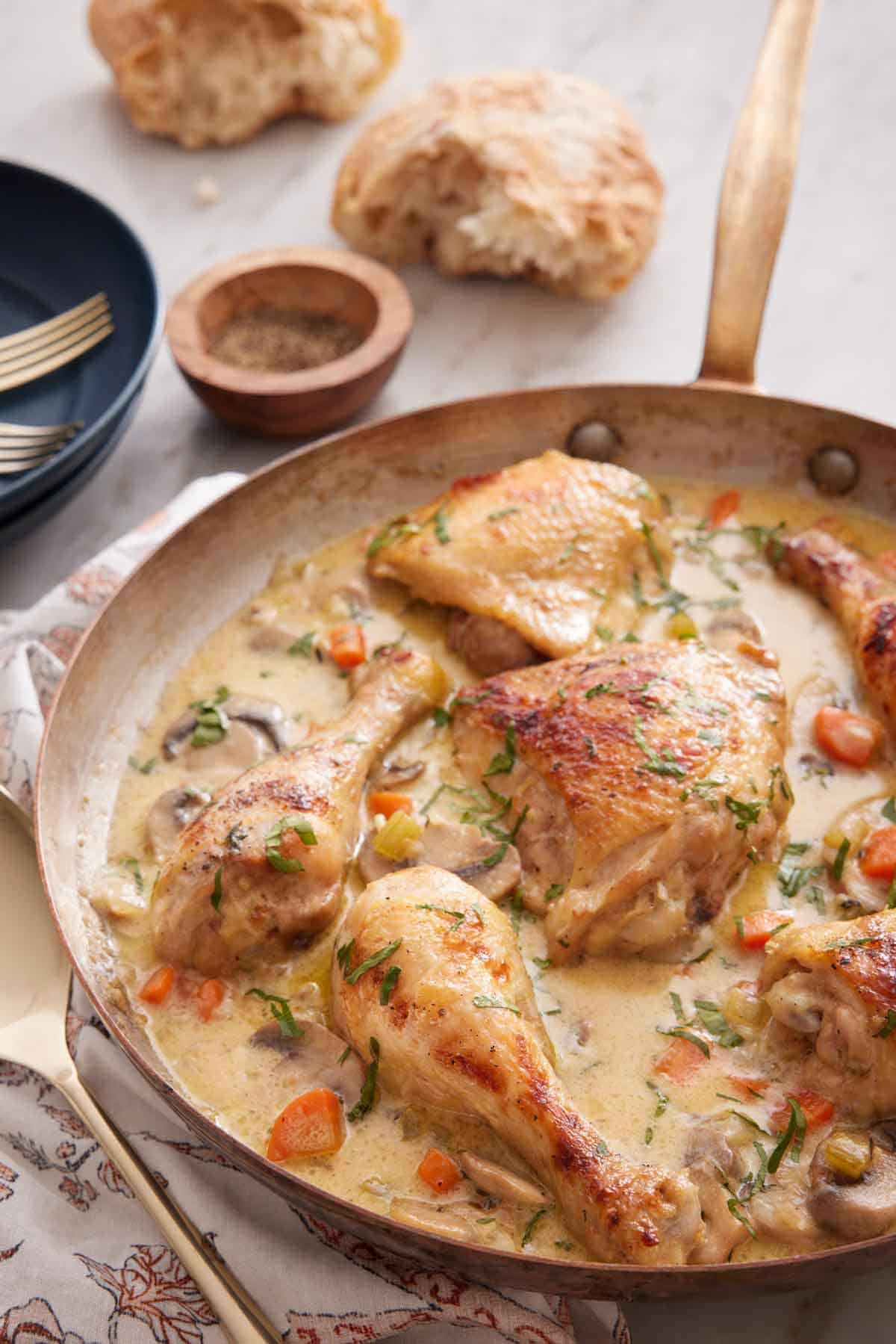 A skillet of chicken fricassée with torn bread in the background.