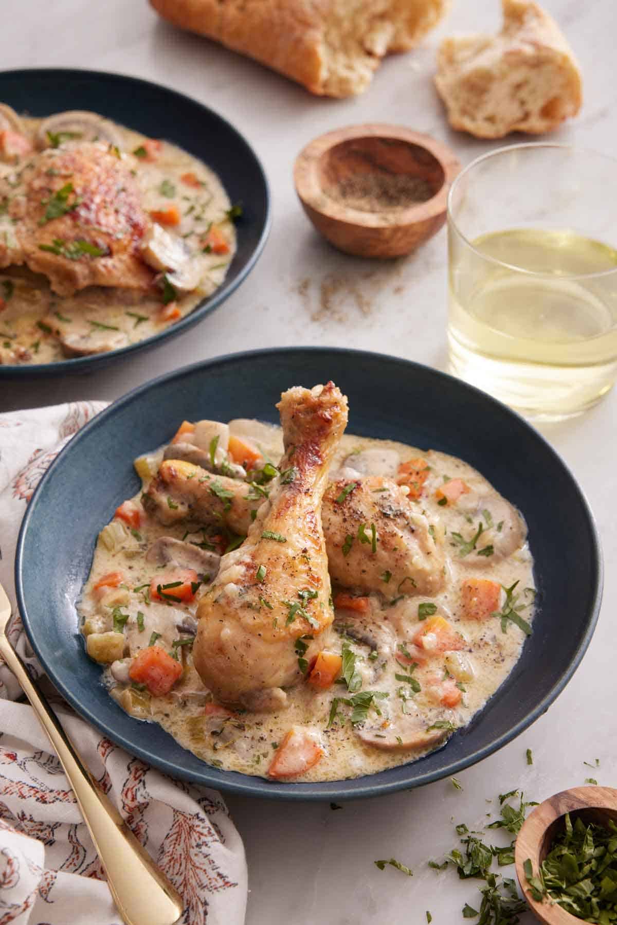 Two plates of chicken fricassée with one in the front and center with a glass of wine and bread in the background.