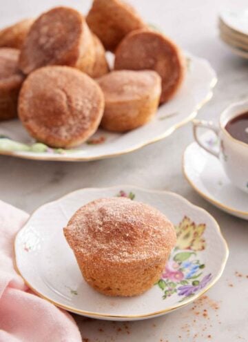 A plate with a cinnamon muffin with a platter in the back along with coffee.