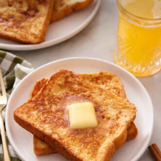 Pinterest graphic of a plate with two pieces of french toast with a pat of butter on top. Orange juice and more french toast in the background.