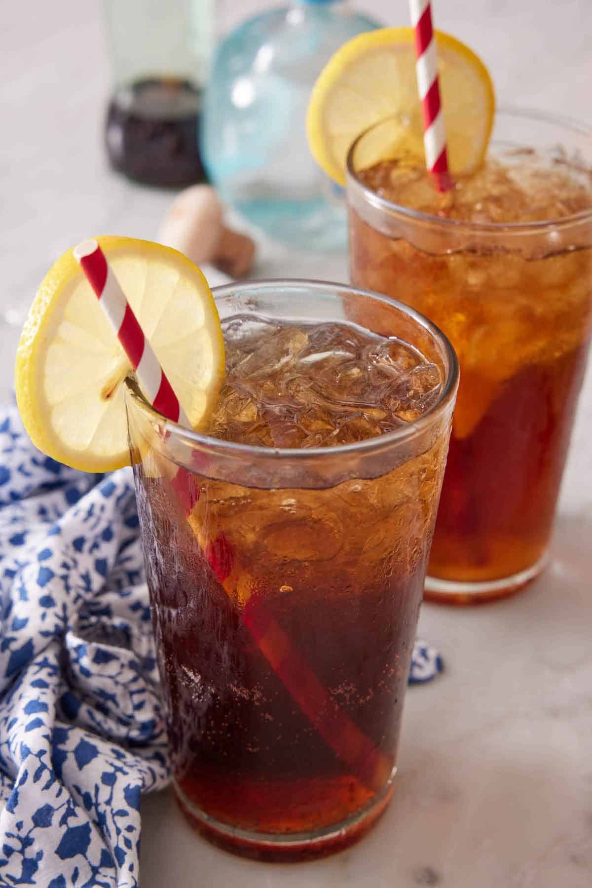 Two glasses of Long Island Iced Tea with straws and a slice of lemon on each rim.