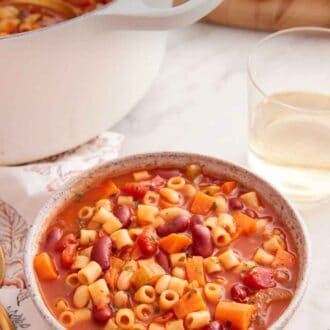 Pinterest graphic of a bowl of pasta fagioli with a pot and glass of wine in the background.