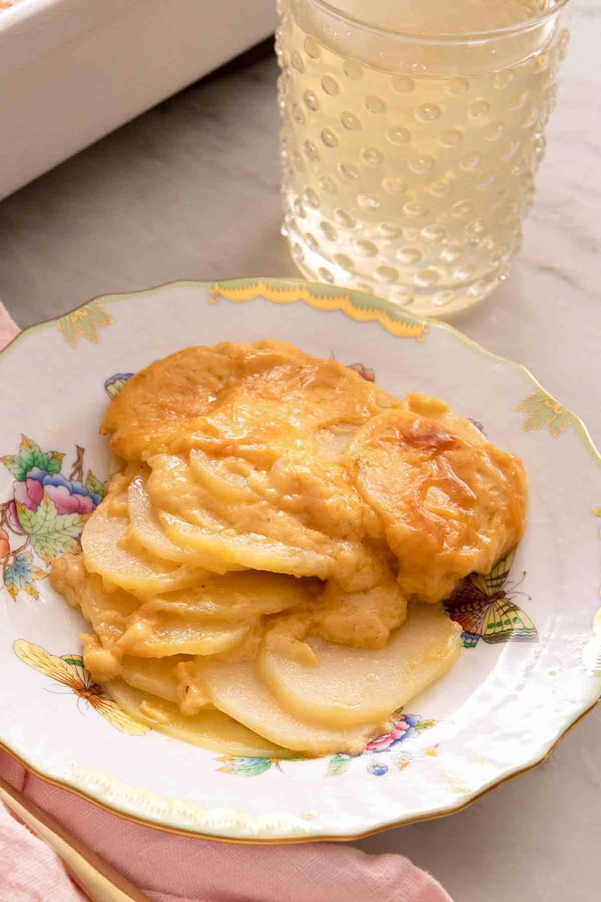 A plate of potatoes au gratin with a drink in the background.