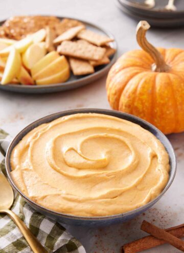 A bowl of pumpkin dip with crackers, apples, and pumpkin in the background.