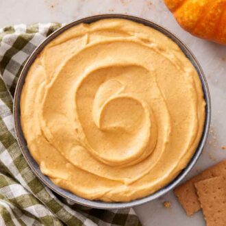 Overhead view of pumpkin dip in a bowl and some crackers, a linen napkin, and a pumpkin off to the side.