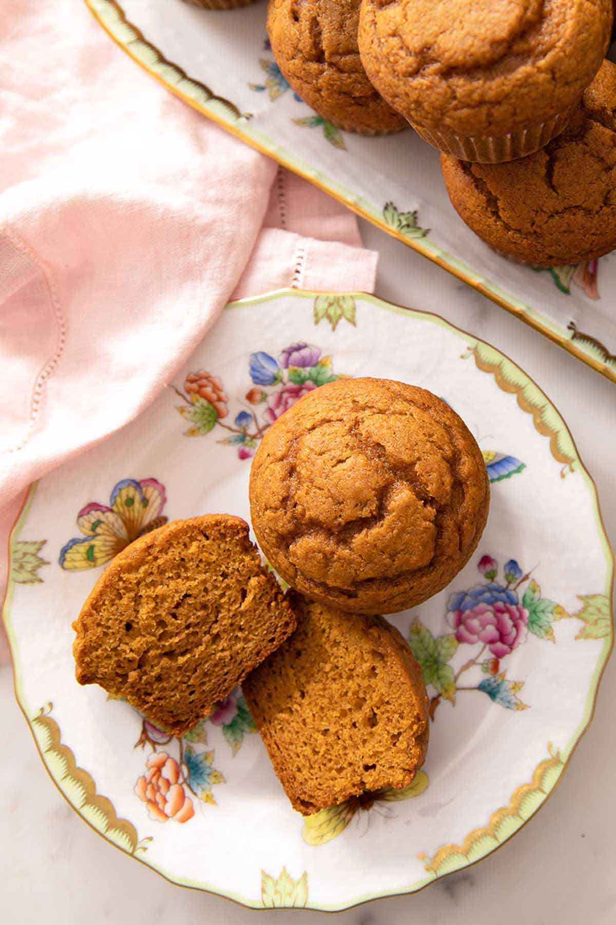 A plate with one pumpkin muffin cut in half, showing the interior, beside a full muffin.