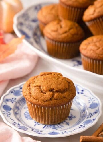 A pumpkin muffin on a plate with more on a platter in the background.