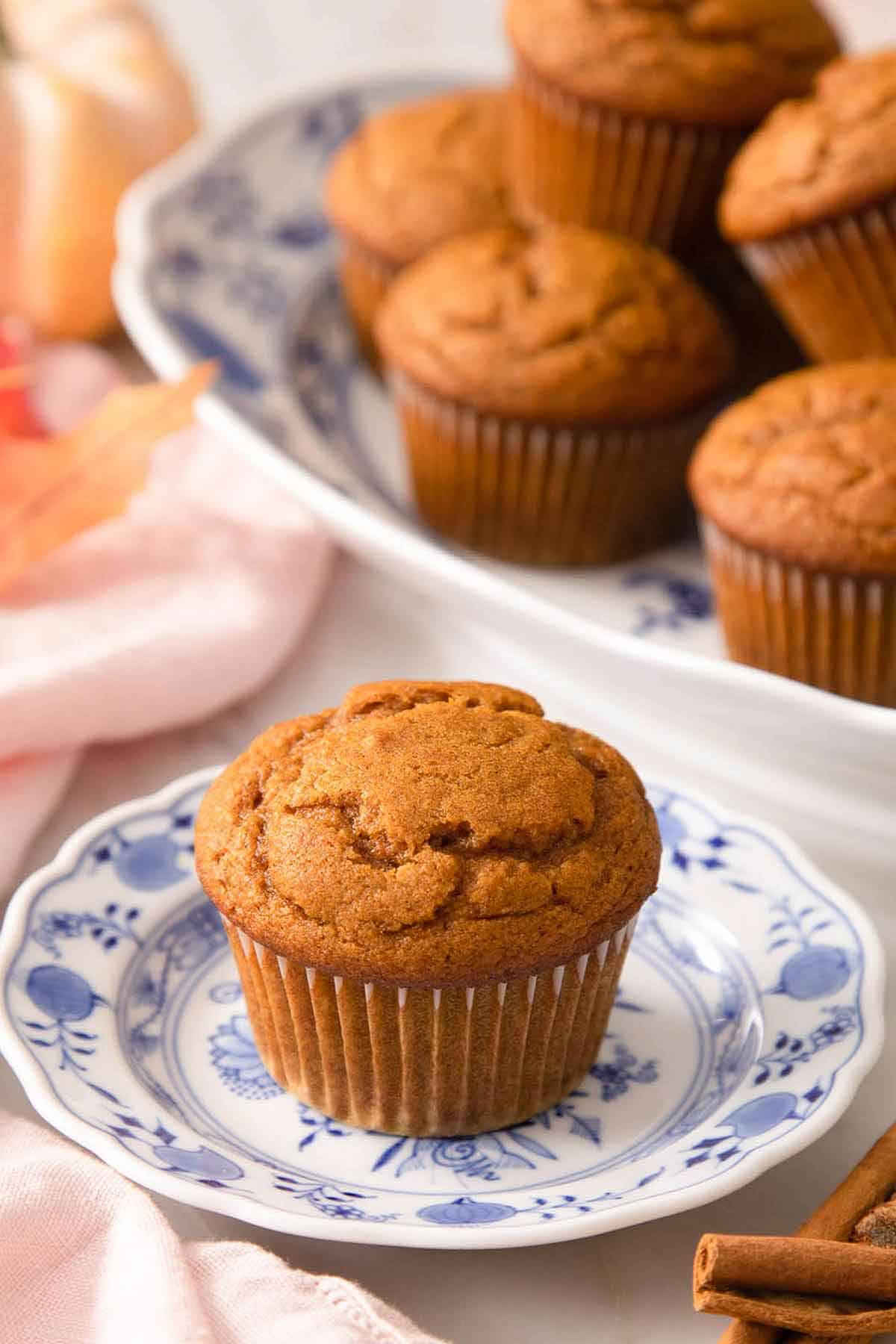 A pumpkin muffin on a plate with more on a platter in the background.