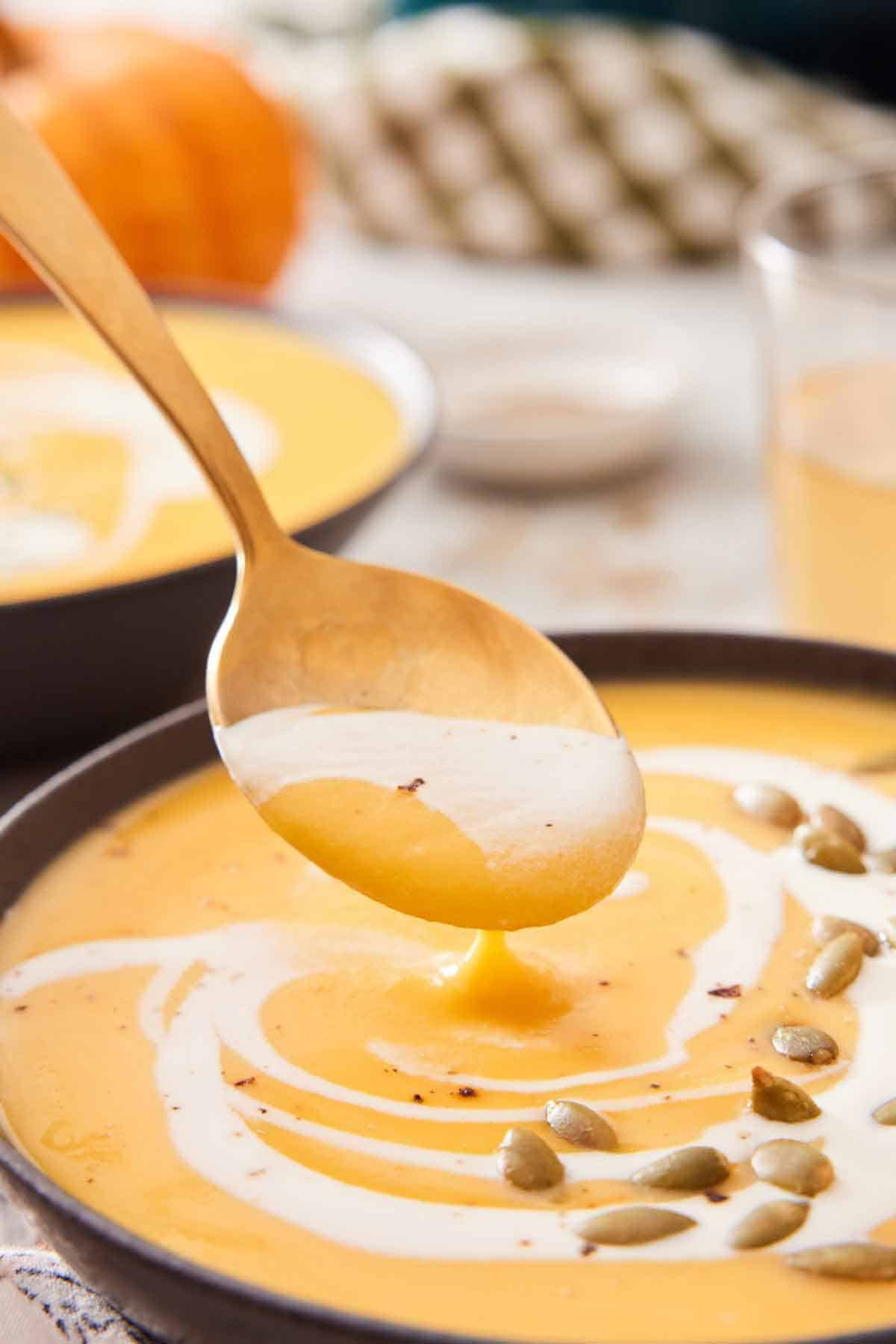 A spoonful of pumpkin soup lifted up from a bowl.
