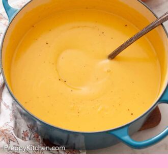 Pinterest graphic of a large pot of pumpkin soup with a ladle inside. Some bowls, spoons, and a pumpkin in the background.