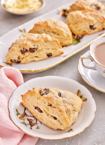 A plate with a scone studded with dried cranberries with additional scones in the background.