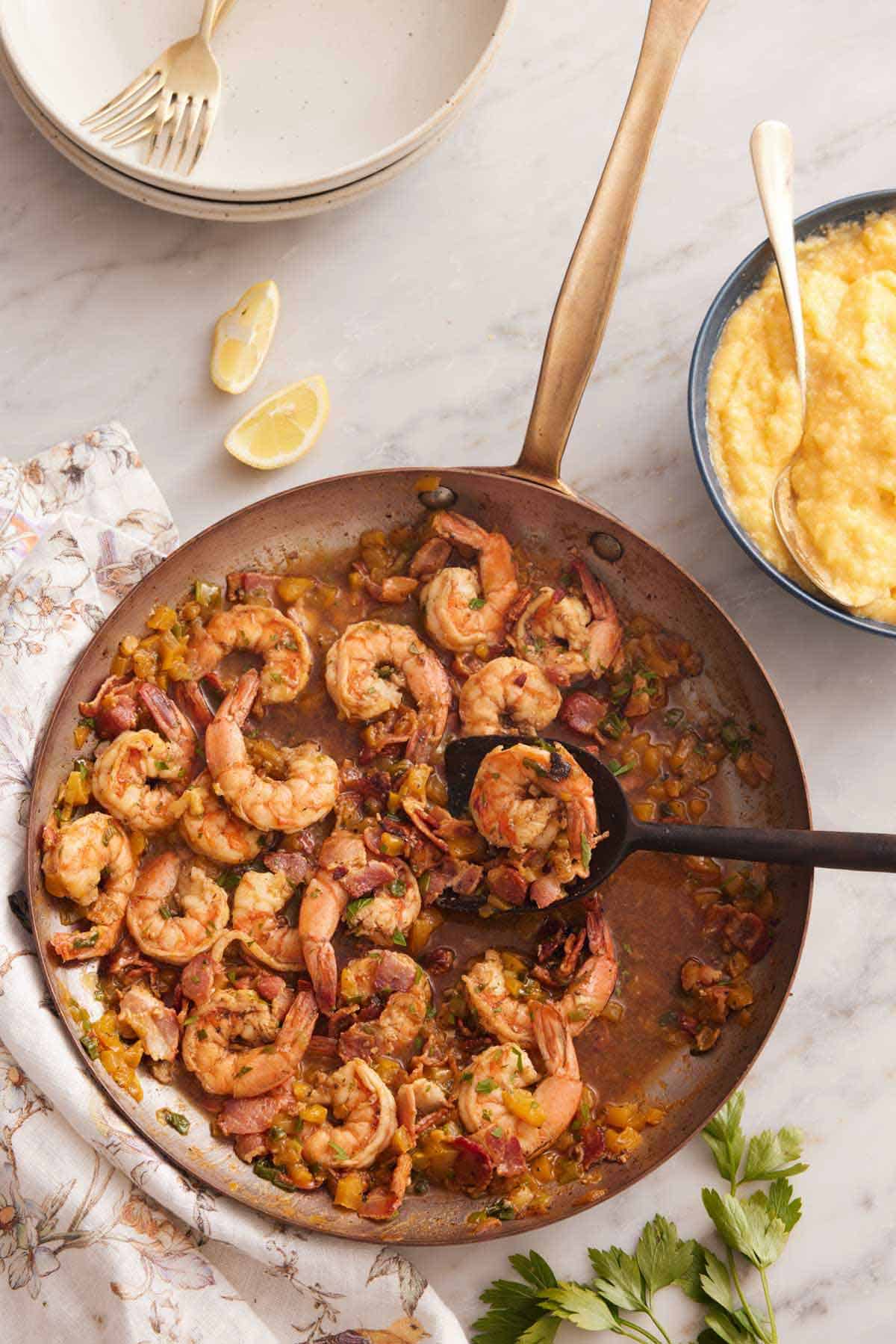 Overhead view of a skillet of cooked shrimp and a bowl of grits off to the side.