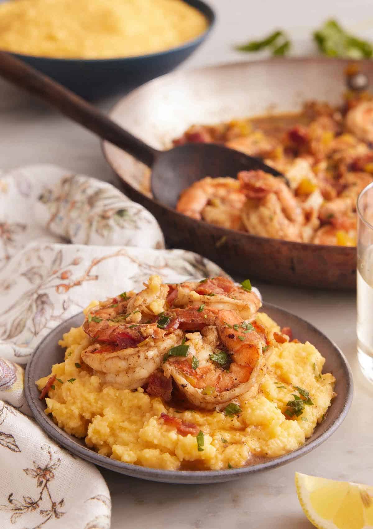 A bowl of shrimp and grits with a skillet of shrimp and bowl of grits in the background.