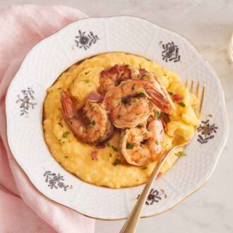 Overhead view of a plate of shrimp and grits with a glass of wine to the side.