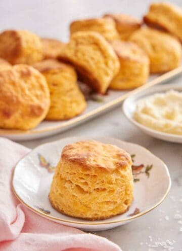 A plate with a sweet potato biscuit with a plate of butter and platter of biscuits in the background.