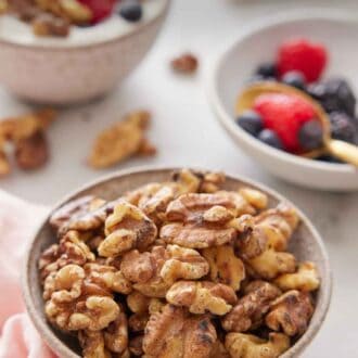 Pinterest graphic of a bowl of toasted walnuts with some berries in the background along with a bowl of yogurt with toasted walnuts and berries.