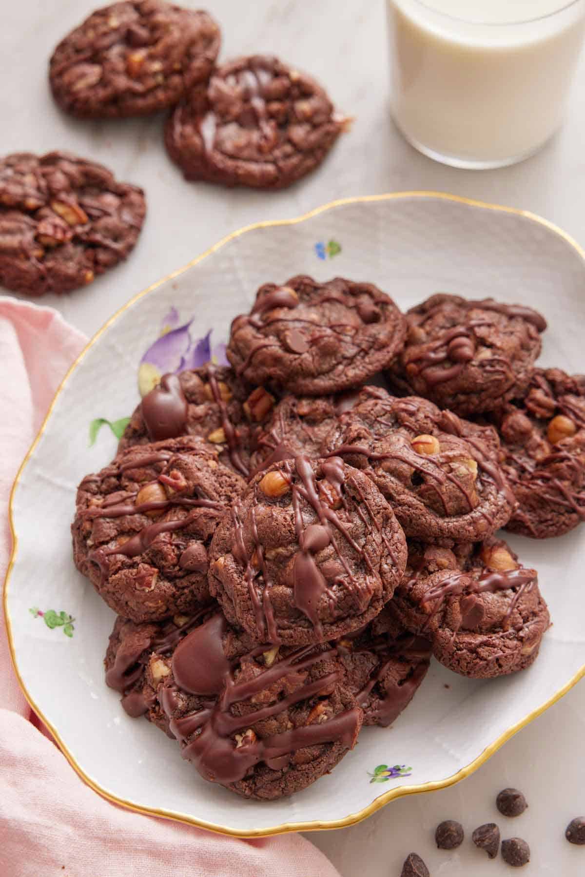A platter of turtle cookies with a glass of milk and three cookies on the table in the background.