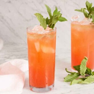 Two glasses of zombie cocktail with mint garnishes with mint on the counter and a bottle of rum in the background.