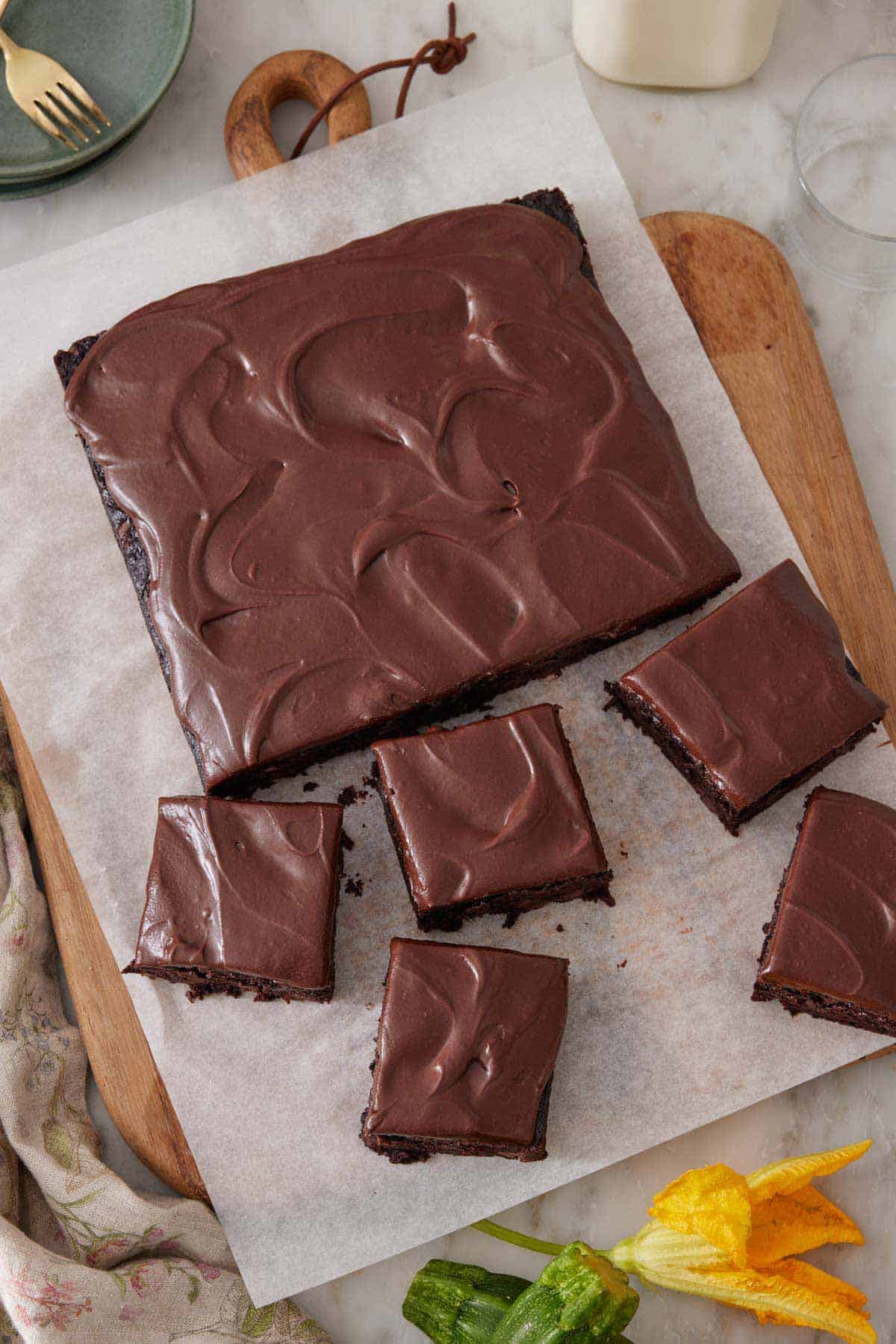 Overhead view of a slab of zucchini brownies on a lined cutting board with five pieces cut.