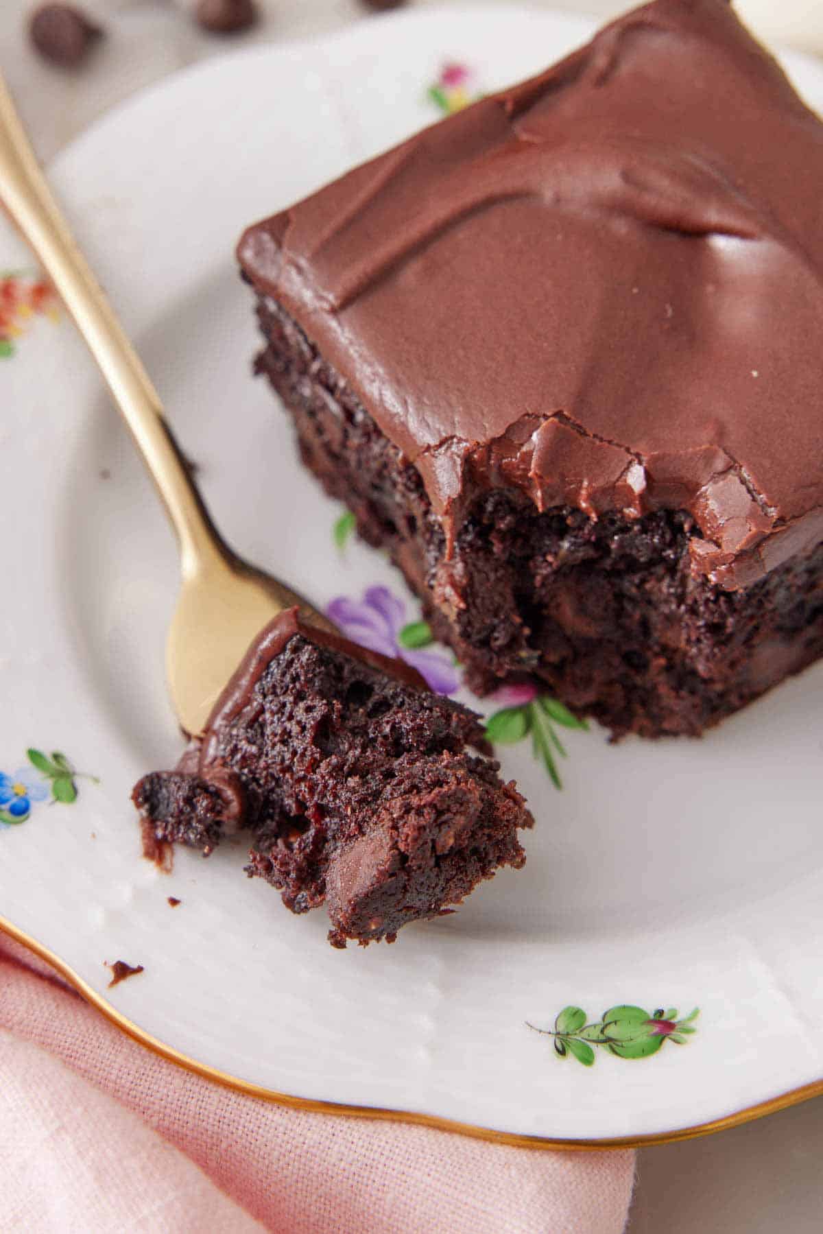 A forkful of zucchini brownie on a plate beside the rest of the brownie.
