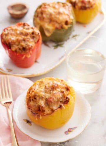 A plate with a serving of air fryer stuffed pepper with a glass of water and additional stuffed peppers in the background.