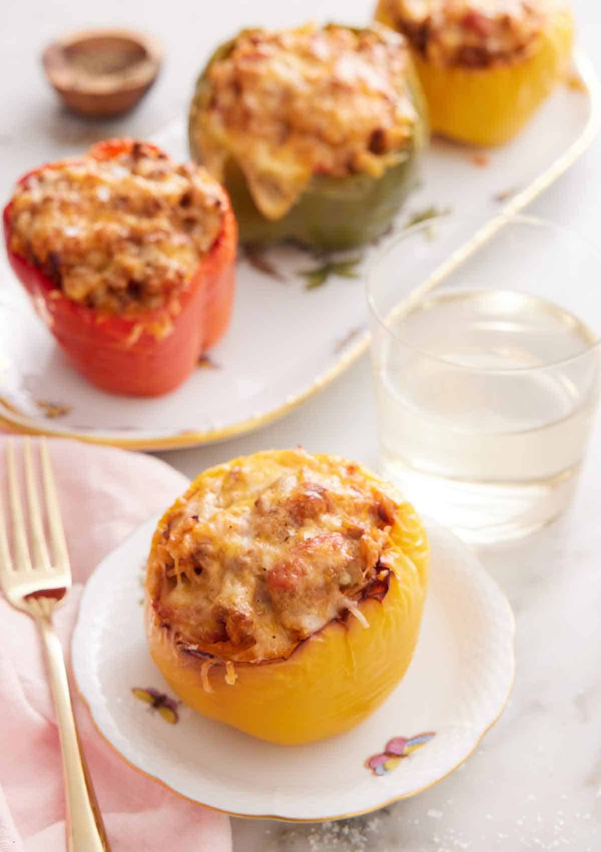 A plate with a serving of air fryer stuffed pepper with a glass of water and additional stuffed peppers in the background.