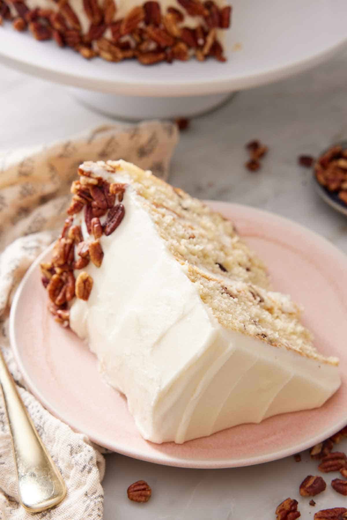 A slice of butter pecan cake on a pink plate with pecans pressed onto part of the frosting.