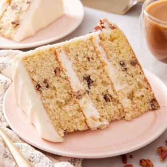 A slice of butter pecan cake on a plate, showing the layers with frosting between them. Coffee in the background.