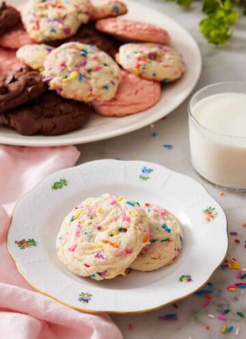 A plate with two cake mix cookies with a glass of milk and additional cookies in the background.