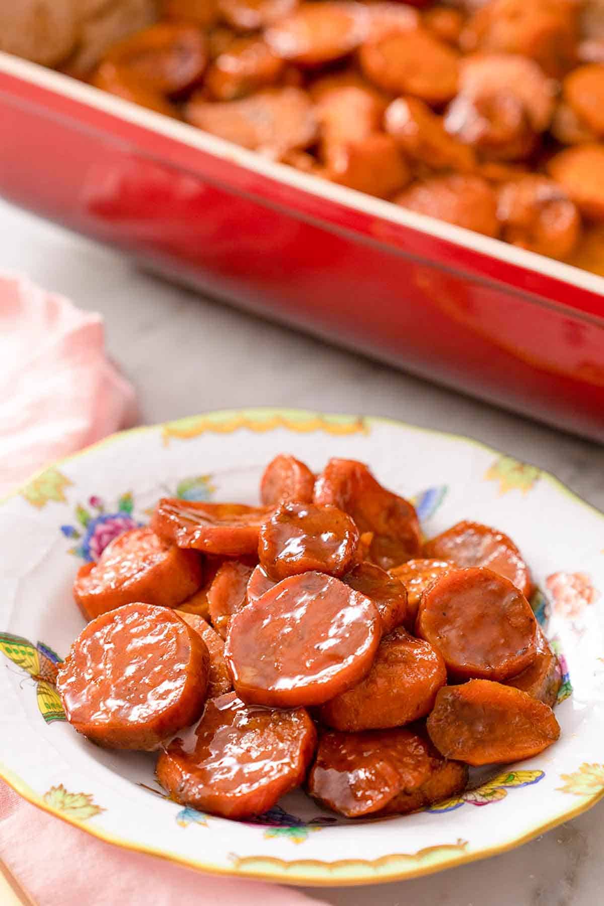 A plate of candied yams with a red casserole dish behind it.