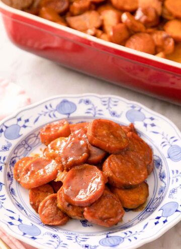 A plate with a serving of candied yams. Red baking dish with the rest in the background.