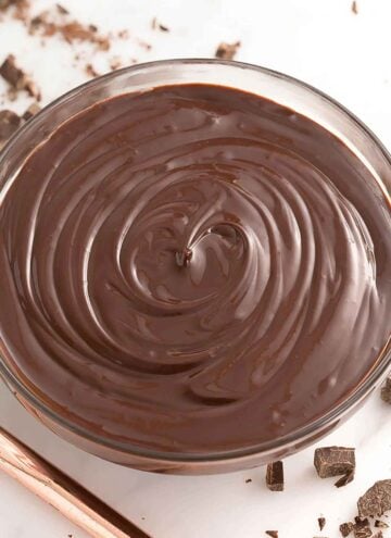 Overhead view of a bowl of chocolate ganache with chopped chocolate off to the side.