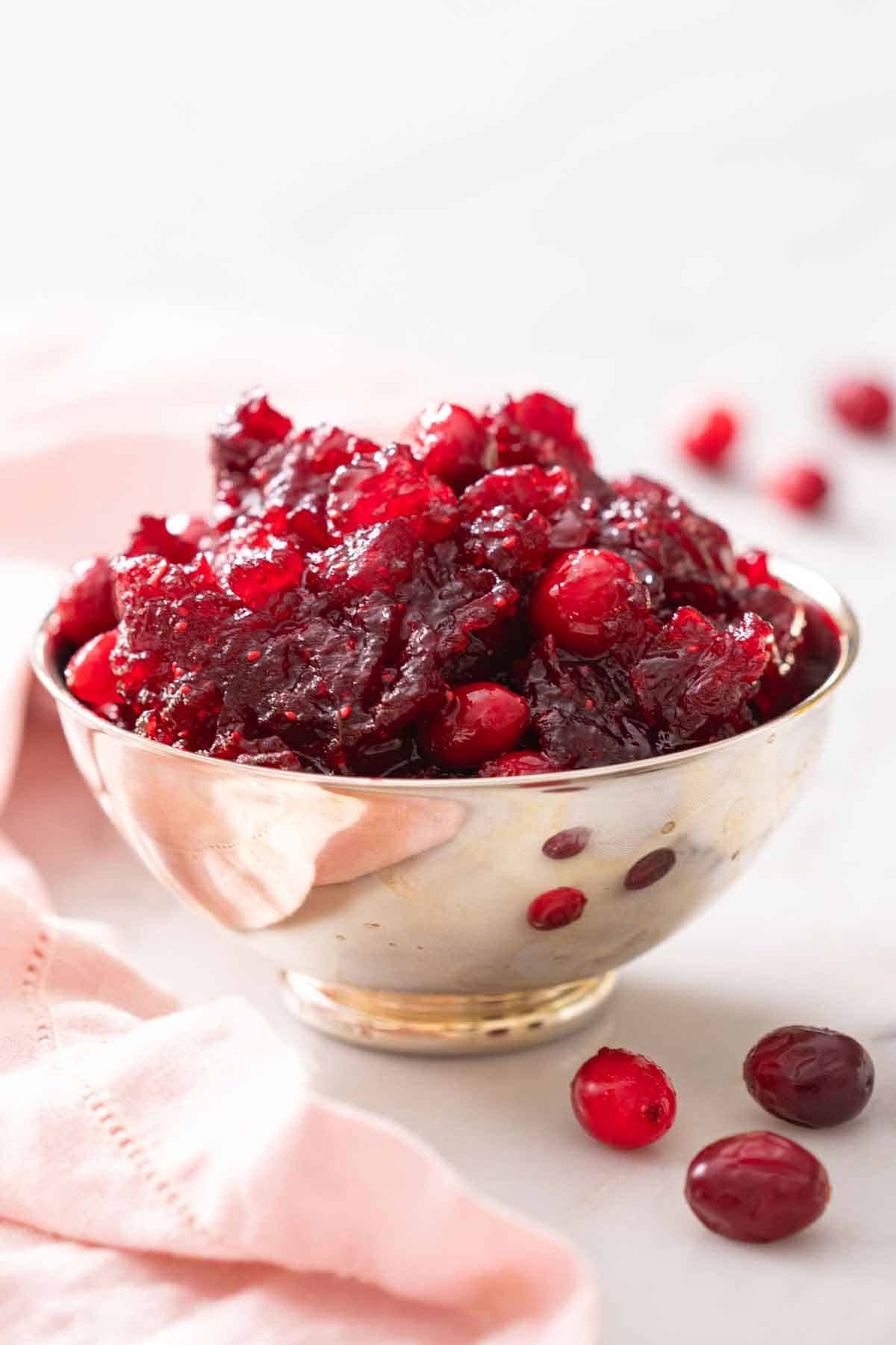 A bowl of cranberry sauce with some cranberries scattered around.