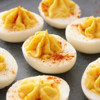 A platter of multiple deviled eggs topped with paprika.
