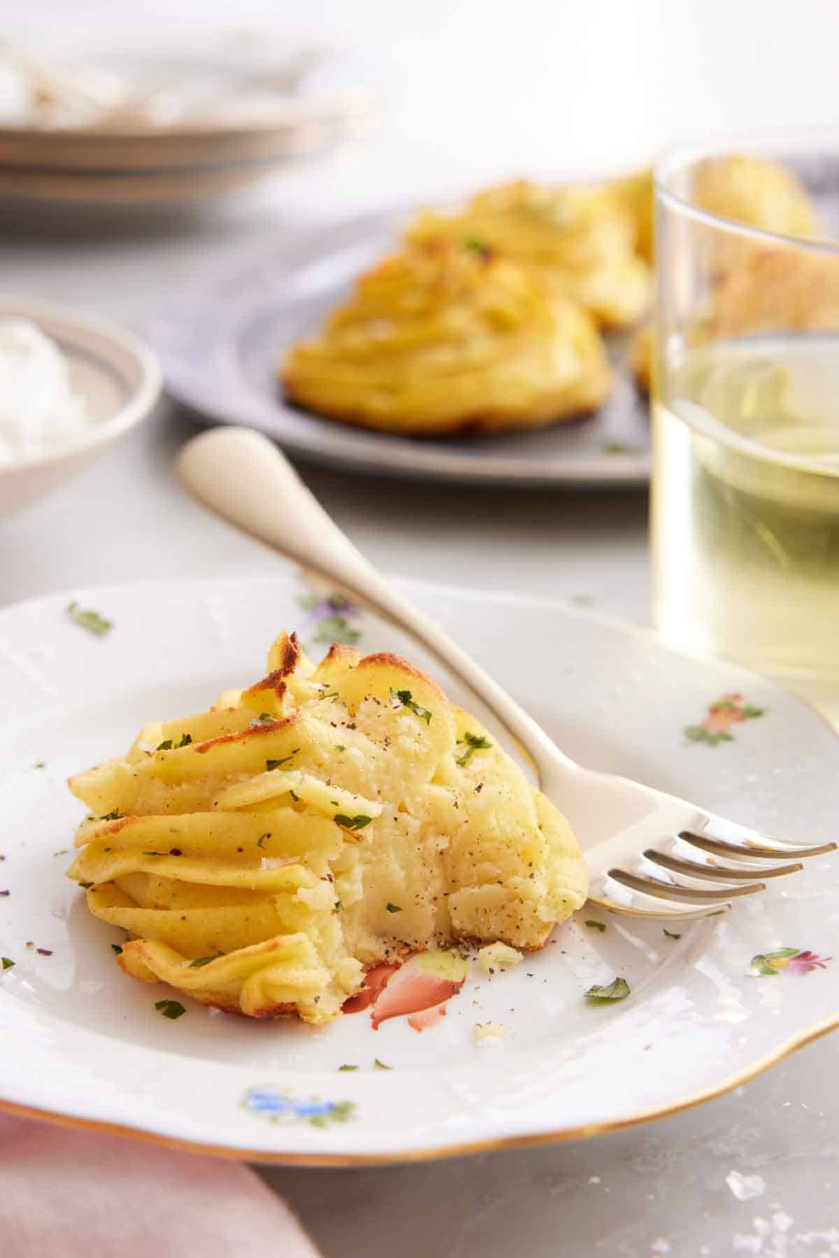 A plate with a serving of duchess potato with a bite taken out. A fork on the plate.