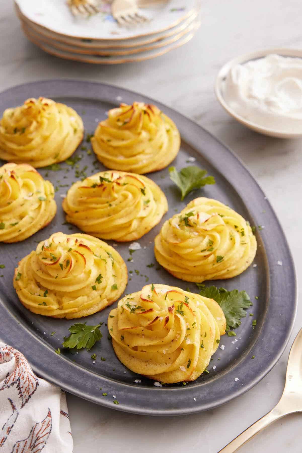 A platter with multiple servings of duchess potatoes topped with parsley and flaky salt.
