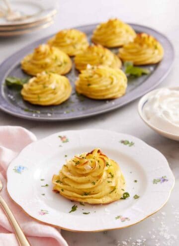 A plate with a serving of duchess potatoes with a platter with more in the background.