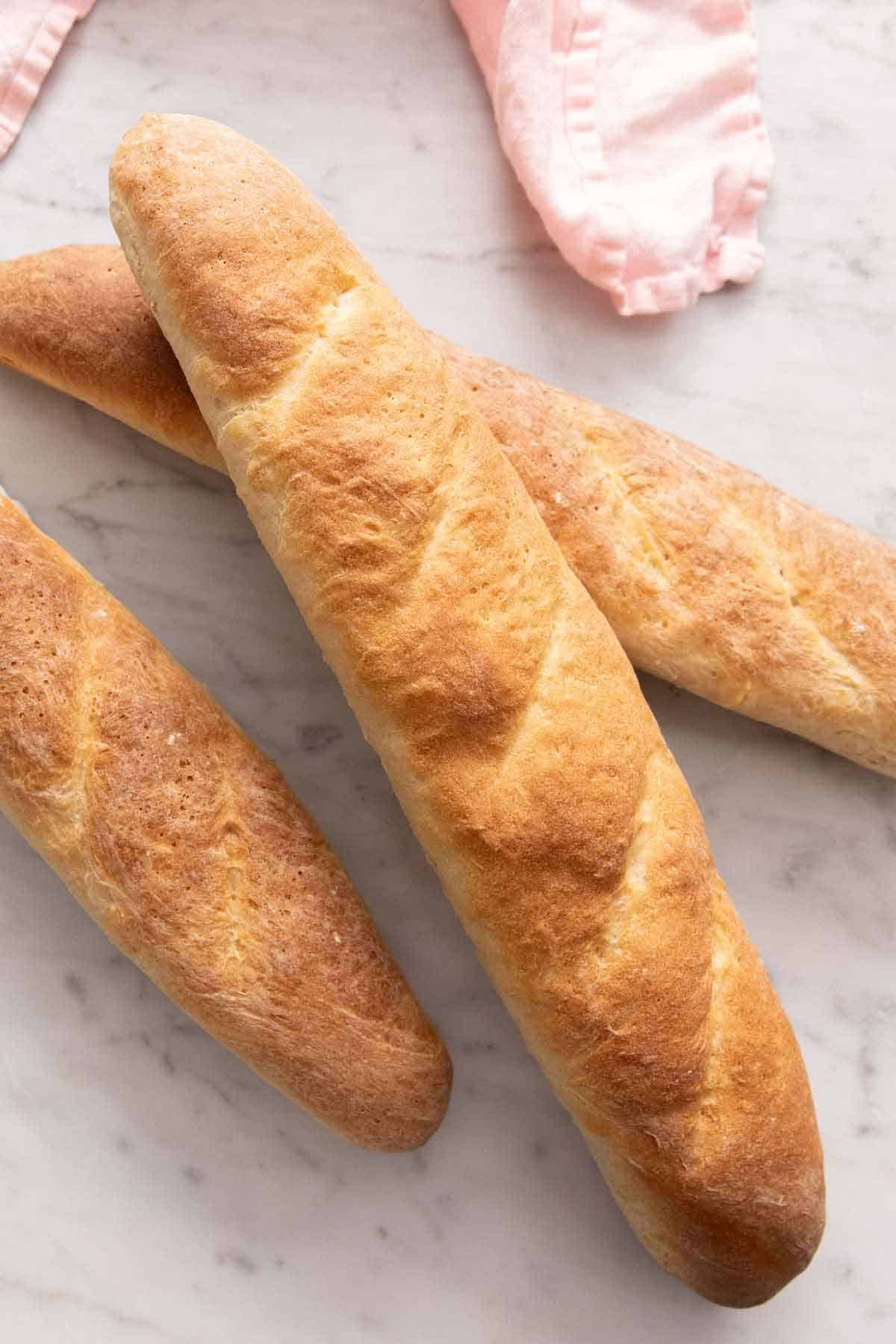 Three loaves of French bread on a marble surface.