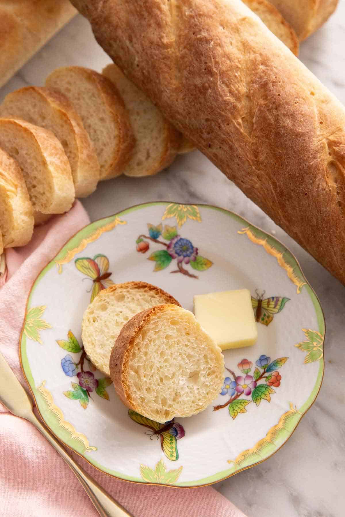 A plate with two slices of French bread with a knob of butter surrounded by more loaves of French bread.