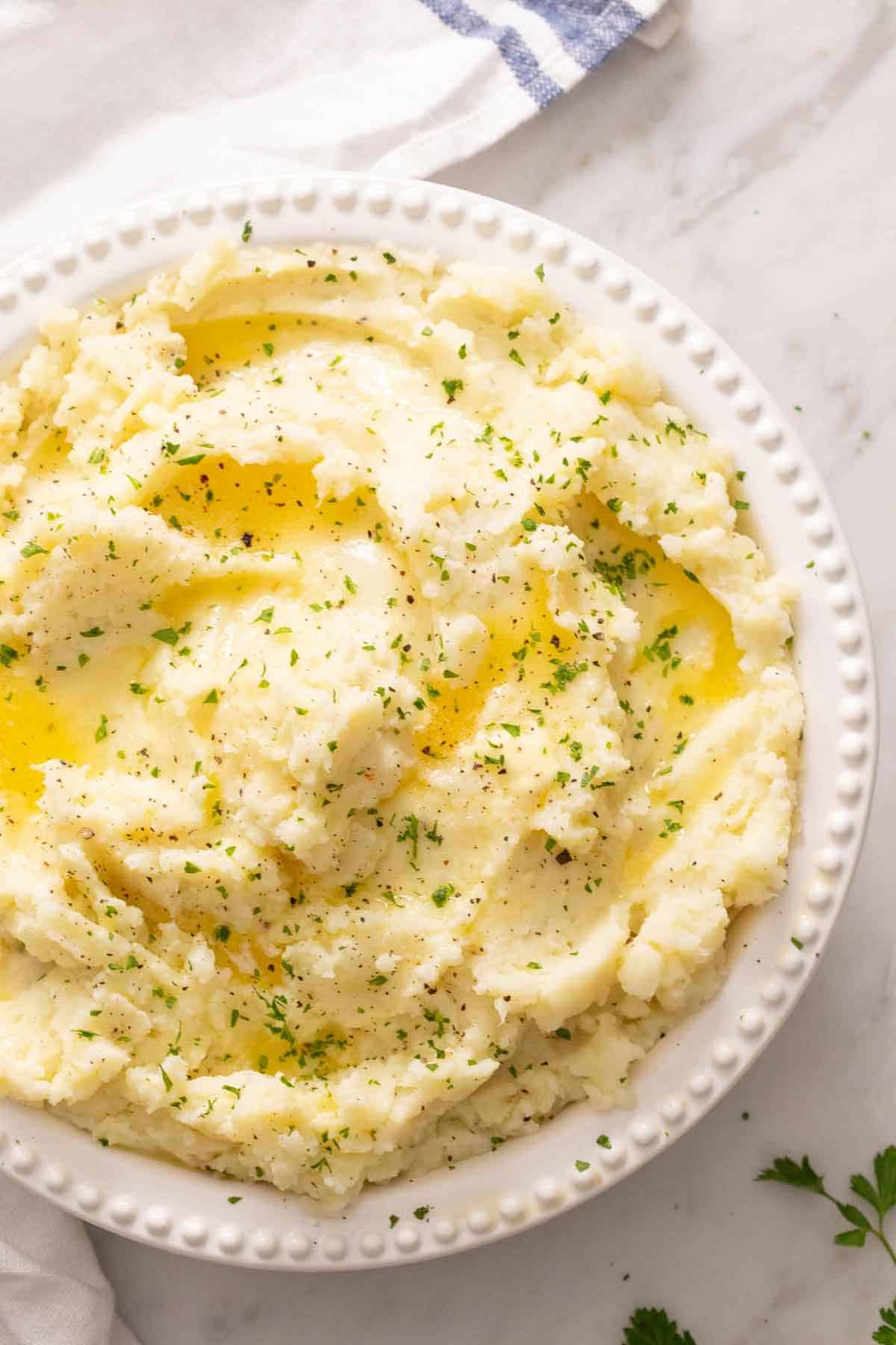 Overhead view of a bowl of mashed potatoes topped with melted butter and herbs.