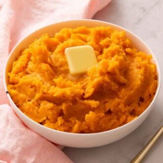 A bowl of mashed sweet potatoes with a knob of slightly melted butter on top with a spoon on the side.