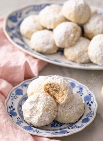 A plate with multiple Mexican wedding cookies, one on top with a bite taken out.