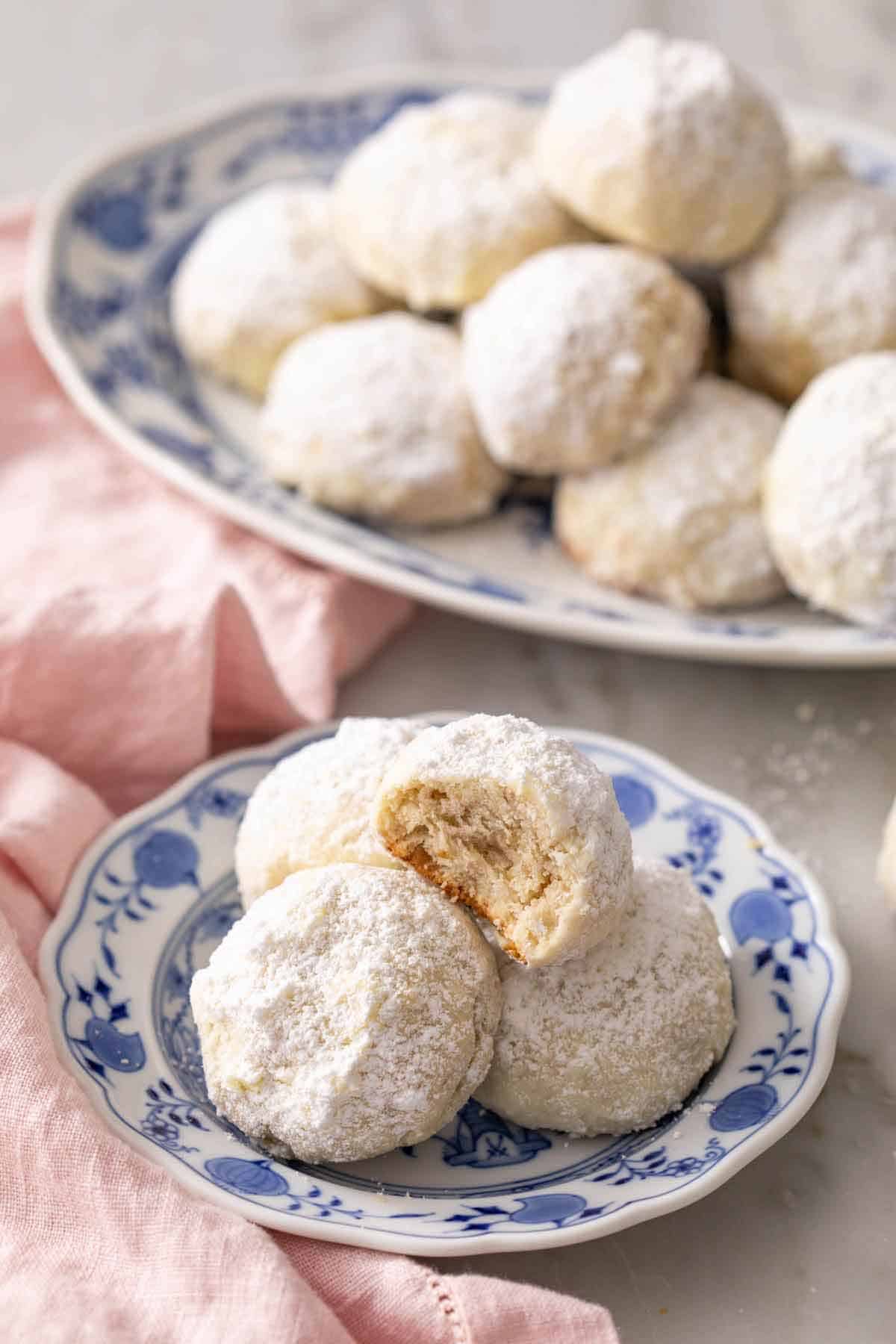 A plate with multiple Mexican wedding cookies, one on top with a bite taken out.