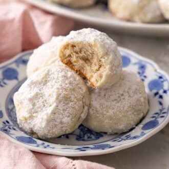 A plate with a handful of Mexican wedding cookies with one on top with a bite taken out.