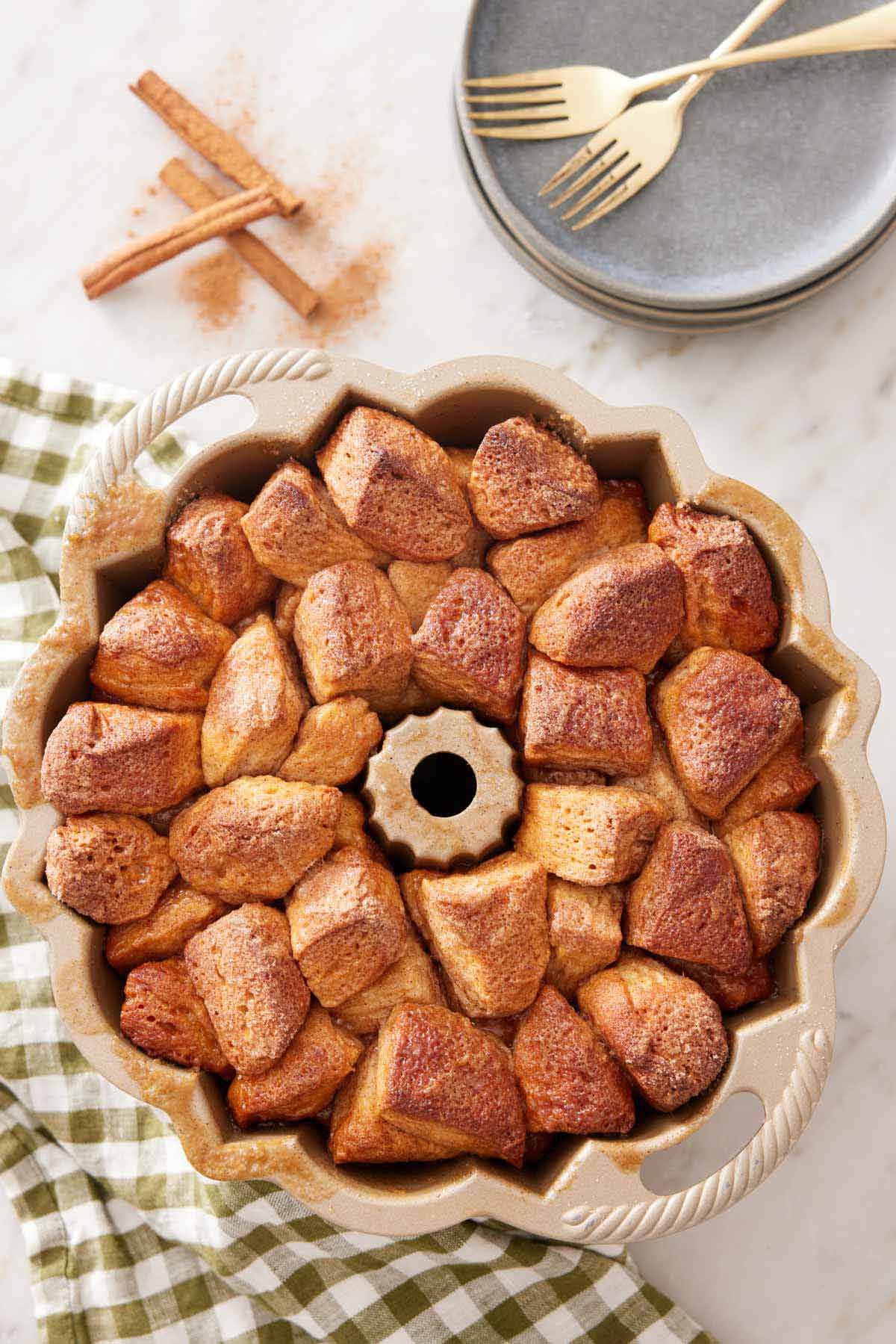An overhead view of monkey bread in the bundt pan. Stack of plates, forks, and cinnamon sticks beside it.