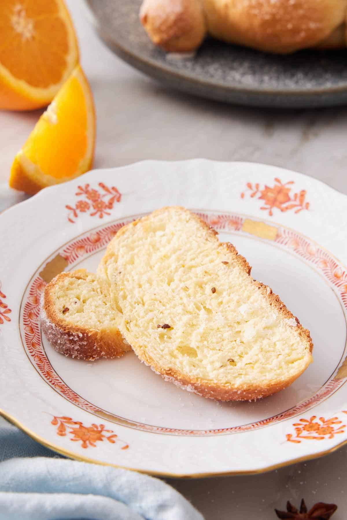 A plate with a slice of Pan de Muerto with a sliced orange in the background.