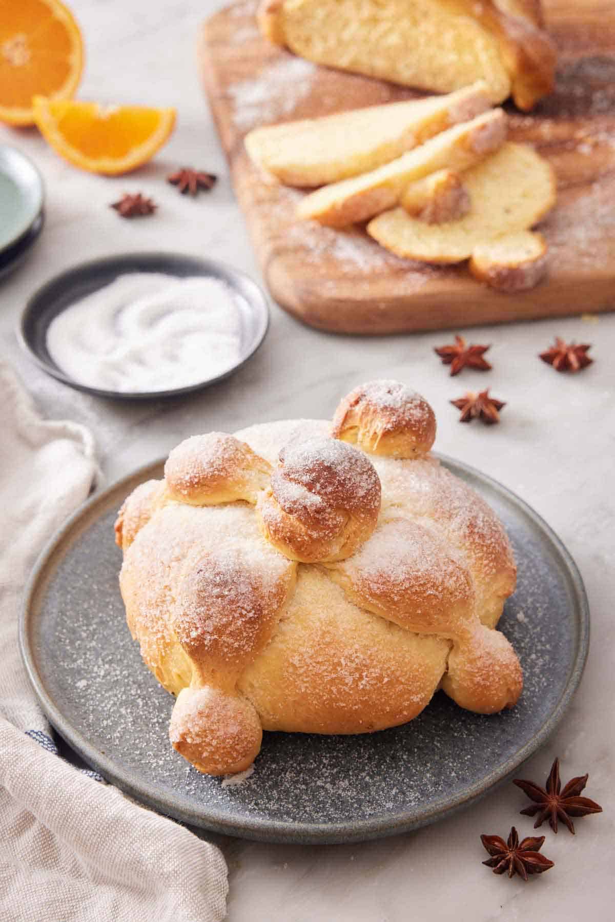 A loaf of Pan de Muerto with a wooden serving board in the back with sliced bread.