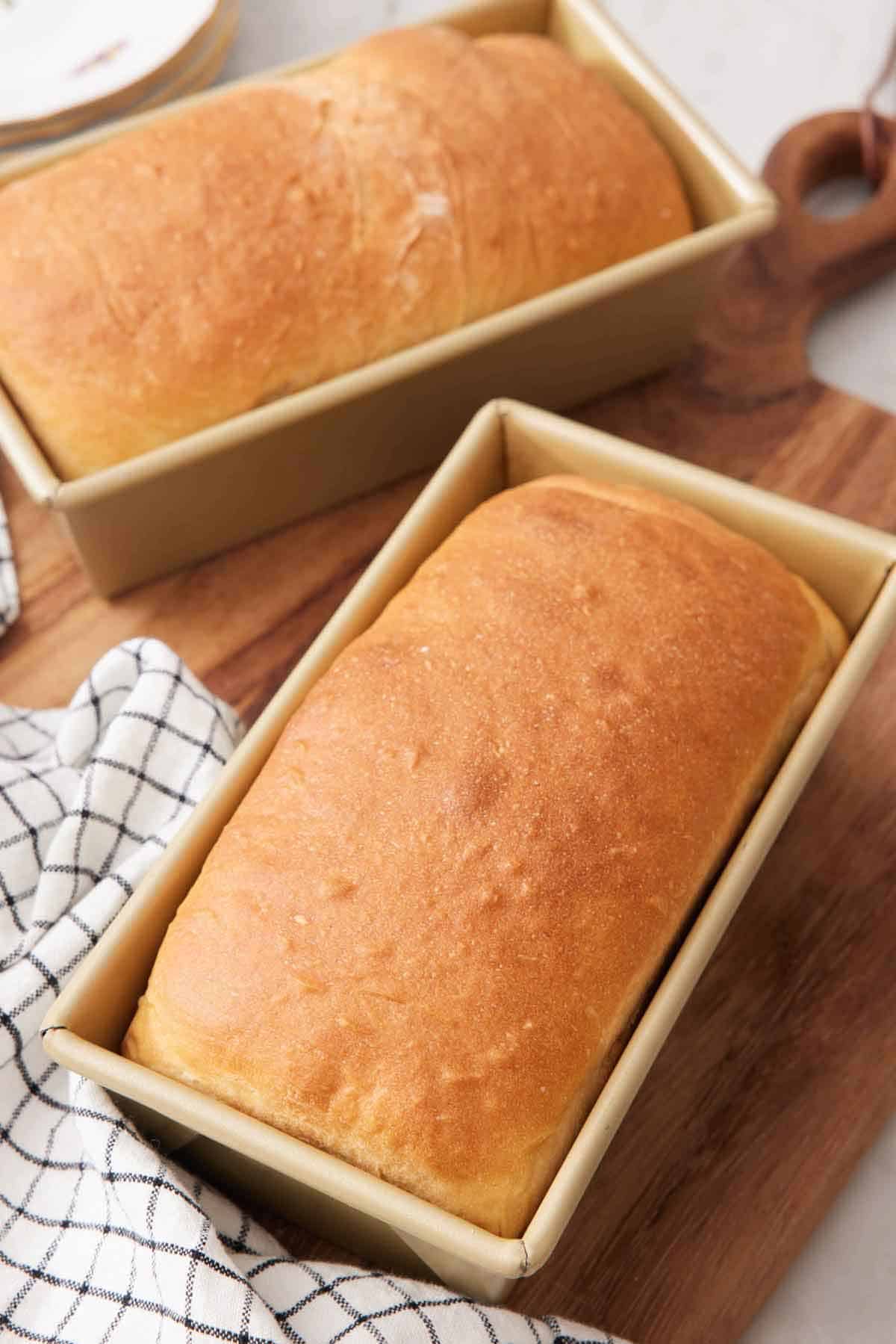 Two loaves of potato bread in their baking dishes on a wooden board.