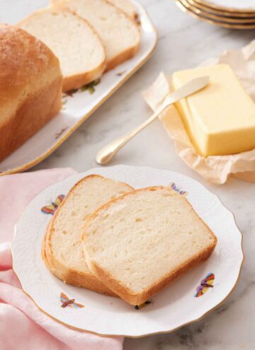 A plate with two slices of potato bread with butter and the rest of the bread in the background.