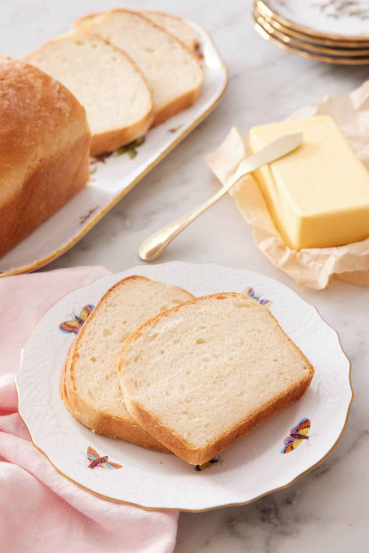 A plate with two slices of potato bread with butter and the rest of the bread in the background.